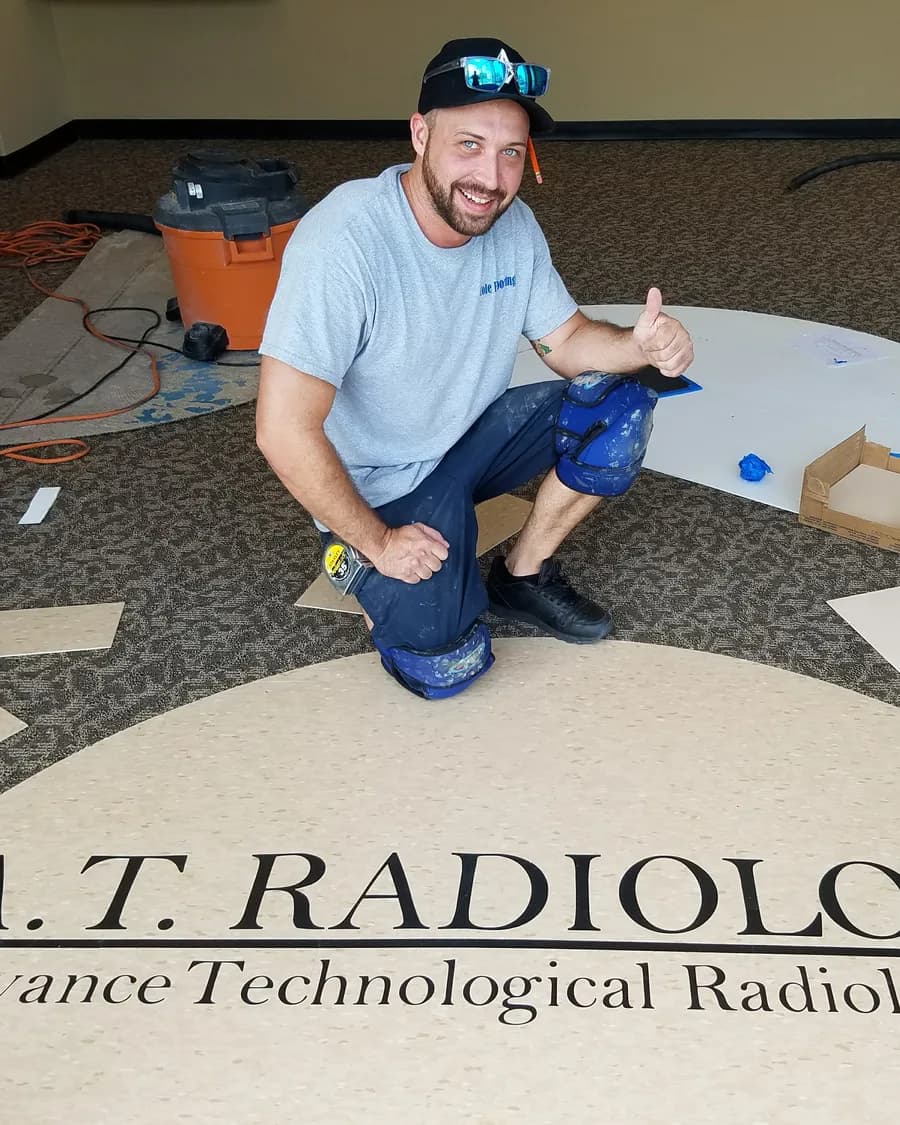 Travis Cole kneeling on a custom logo floor his crew installed at a radiology office